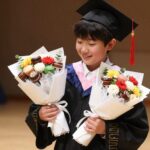 졸업식에서 아이가 츄파춥스 사탕부케와 비누꽃다발을 들고 웃고 있는 모습